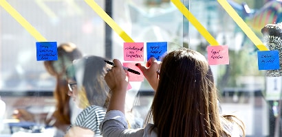 Kvinna som sätter Post-it® Super Sticky Note, 76 mm × 76 mm på en glasvägg för att dela anteckningar med andra teammedlemmar eller projektgrupper